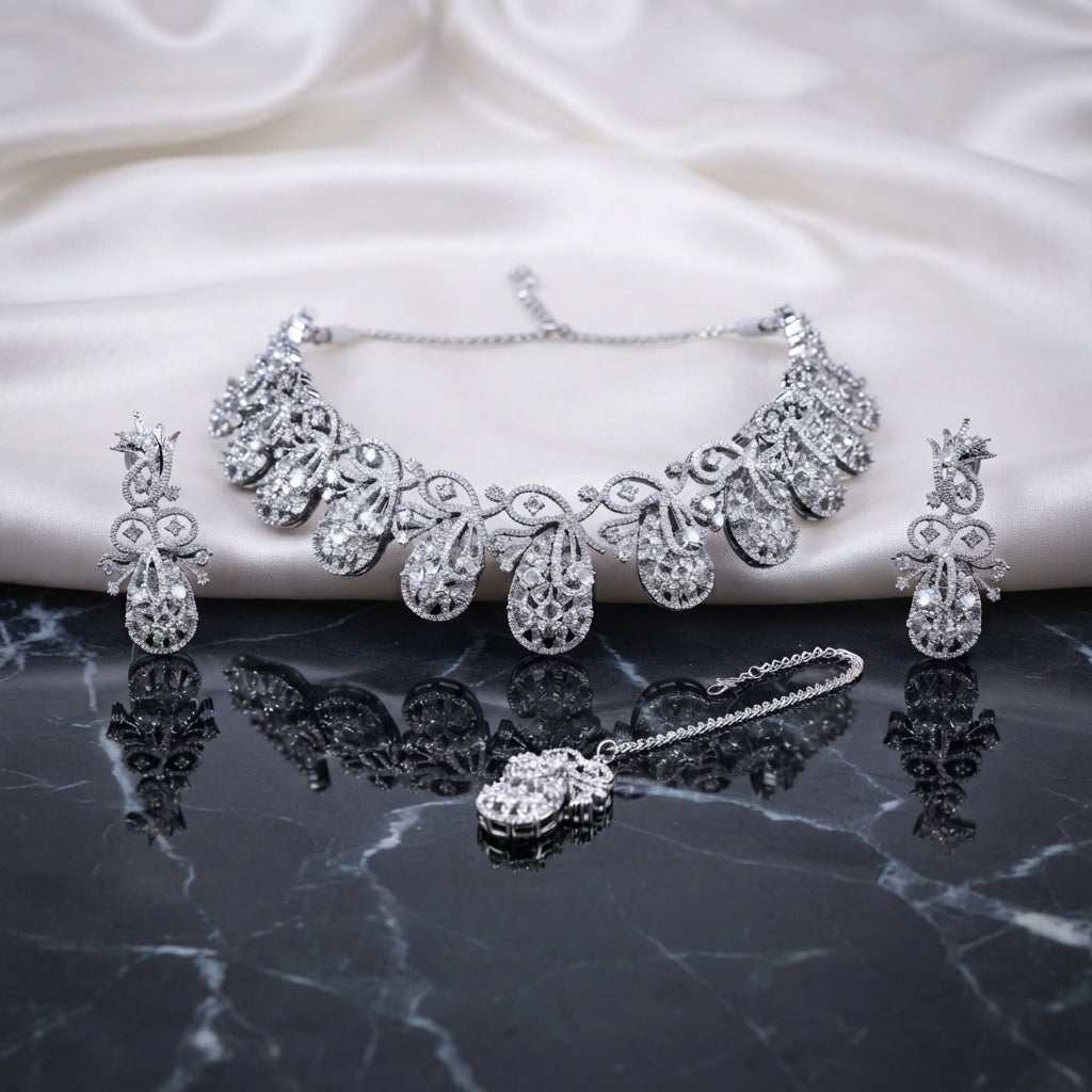 Silver White CZ Peacock Feather Filigree Choker Earrings and Maang Tikka Bridal Set flat lay on dark marble with white ivory satin backdrop showing rhodium silver 3-piece bridal set with peacock feather open filigree choker drop earrings and maang tikka