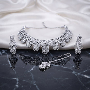 Silver White CZ Peacock Feather Filigree Choker Earrings and Maang Tikka Bridal Set flat lay on dark marble with white ivory satin backdrop showing rhodium silver 3-piece bridal set with peacock feather open filigree choker drop earrings and maang tikka
