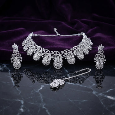 Silver White CZ Peacock Feather Filigree Choker Earrings and Maang Tikka Bridal Set flat lay on dark black marble with purple velvet backdrop showing 7 graduated peacock feather filigree teardrop motifs with scrolling vine white CZ and oval solitaire centres matching drop earrings and maang tikka