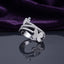 Silver White CZ Triple Pave Band Dual Butterfly Wide Statement Ring angled side view on dark grey mirror surface with deep purple amethyst velvet backdrop showing full band depth and 3D sculptural dual butterfly profile with three parallel open micro-pave white CZ cage-band rails in rhodium silver with mirror reflection below