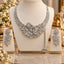 Silver White and Pink CZ Asymmetric Floral Vine Bib Necklace Earrings and Tikka Set displayed on white jewelry stand in luxury boutique setting with white gypsophila flowers and gold mirror backdrop showing 3-piece set with dramatic asymmetric floral vine bib necklace with white CZ tennis chain band and pink CZ flower accents with decorative side chain tassel drop and matching long floral vine drop earrings and tikka