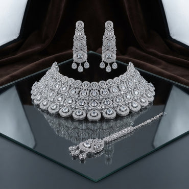 Silver White Polki CZ Grand Medallion Bib Choker Chandelier Earrings & Maang Tikka Grand Bridal Set on mirror surface with dark brown velvet and white drape backdrop