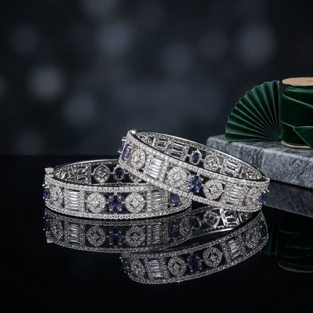 Silver-Tone Wide Art Deco Baguette & Oval Sapphire Blue CZ Openwork Geometric Micro-Pavé Bridal Bangle Set of 2 on black mirror surface with grey concrete stone prop and dark green velvet fan backdrop
