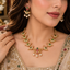 Model wearing a South Indian-style gold-tone bird motif necklace and matching earrings with pink and green accents and white pearl-look drops.