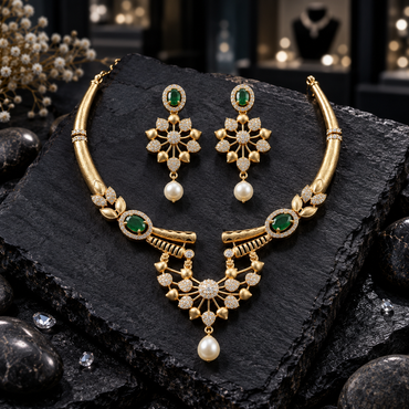 Gold-tone necklace with green oval halo accents, leaf details and an openwork fan-style centre, beside matching earrings with cream pearl-look drops on dark slate.