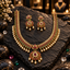 South Indian-style gold-tone necklace and earrings with pink-red and green accents, clear details, a floral teardrop pendant and white pearl-look fringe.