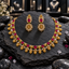 Gold-tone South Indian-style necklace with vivid pink oval accents, small green details, embossed oval charm fringe and cream pearl-look accents, with matching earrings.