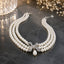 Three-Strand White Pearl Choker Necklace with Silver Pavé CZ Bow & Teardrop Pearl Pendant on dark marble surface with baby's breath flowers and crystal candle holder backdrop