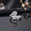 Toi et Moi Double Oval CZ Milgrain Halo Baguette Bypass Ring in Silver — rhodium-plated silver-tone Cartier-inspired Toi et Moi ring with 2 oval white CZ solitaires in individual round CZ milgrain pavé halos in bypass crossover embrace and baguette CZ channel shoulders, on dark grey mirror surface with gold geometric bokeh luxury editorial backdrop