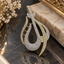 Two-tone curved teardrop pendant with clear accents, gold-tone and silver-tone outlines, openwork crossbars and an elongated hanging loop.