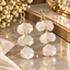 Pair of white pearlescent-look petal drop earrings with textured scalloped edges, three tiers and gold-tone loop-and-bow details.